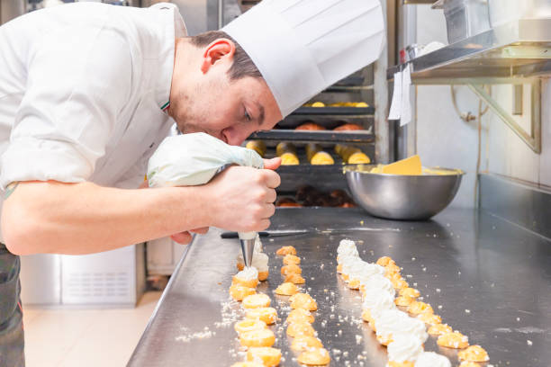 pastry chef filling small pastries with pastry bag pastry chef is preparing small pastries filling them with a icing bag confectioner stock pictures, royalty-free photos & images