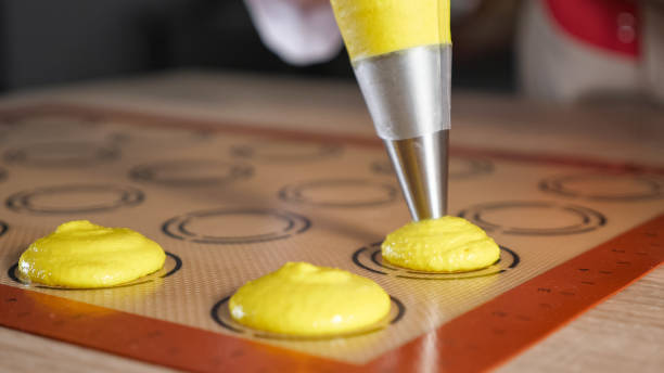 Pastry chef is cooking macaroons. Pouring dough on stencil silicone mat. stock photo