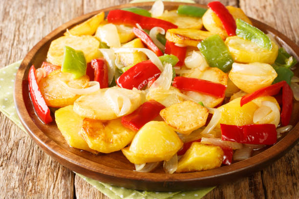 Patatas a lo pobre is a simple potato dish from Andalusian cuisine made of sliced potatoes are fried in olive oil with onion and peppers close up on the table. Horizontal stock photo