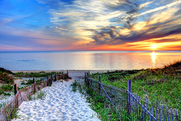 Path with beach fence on Cape Cod Path with beach fence leading to a secluded beach at sunset near Provincetown on Cape Cod. Cape Cod has some of the worlds most beautiful beaches. Cape Cod is famous, worldwide, as a coastal vacation destination with some of New England's premier beach destinations cape cod stock pictures, royalty-free photos & images