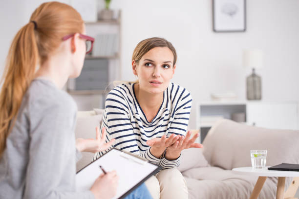 Patient after traumatic events Red haired psychiatrist listening her patient after traumatic events while sitting on beige settee bad news photos stock pictures, royalty-free photos & images