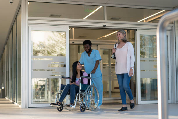 黒人男性看護師が運んだ車椅子で退院する患者 - 退院 ストックフォトと画像