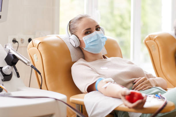 Patient receiving a blood transfusion Portrait of young woman in protective mask looking at camera while lying on the couch and receiving a blood transfusion at hospital blood donation stock pictures, royalty-free photos & images