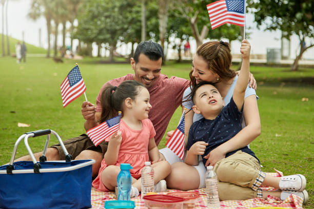 Patriotic Hispanic Family Picnicking at Miami Public Park Young Miami family with 4 and 6 year old children holding American flags while enjoying weekend picnic lunch. labor day stock pictures, royalty-free photos & images