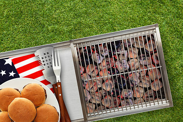 Patriotic Hot Grill with Platted Burgers on Lawn Hot grill with glowing charcoal briquettes on a red, white and blue napkin creates theme for the patriotic holidays of Fourth of July, Memorial Day and Labor Day traditional picnics. memorial day background stock pictures, royalty-free photos & images