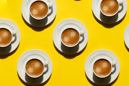 Pattern made of cup of cappuccino on yellow background