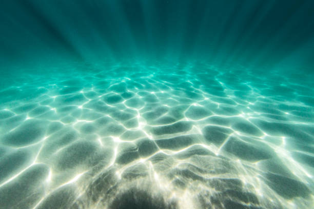 Patterns from light rays reflecting on teal blue ocean floor stock photo