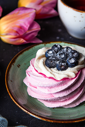 Pavlova cake with blueberries on a plate close-up, tea and pink tulips vertical photo. High quality photo