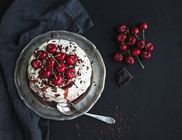 Pavlova cake with fresh cherry, cheese cream and chocolate chips Pavlova cake with fresh cherry, cheese cream and chocolate chips in vintage silver plate over dark grunge background, top view, copy space pavlova dessert photos stock pictures, royalty-free photos & images