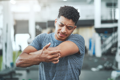 Shot of a young man experiencing elbow pain in a gym