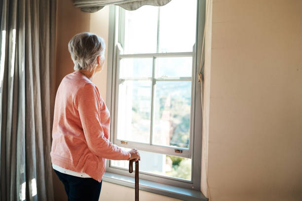 Peace of mind is all we're looking for Shot of a senior woman with a cane looking thoughtfully out of a window at home loneliness stock pictures, royalty-free photos & images