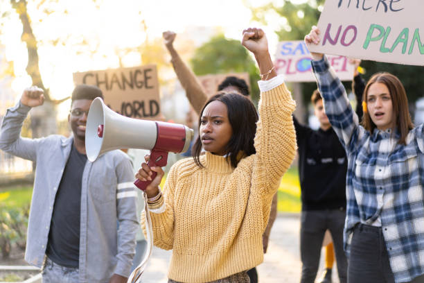 A peaceful protest to protect the environment A multiracial girl uses a megaphone to broadcast about environmental issues while her friends hold banners in the air during a protest in a public park climate action stock pictures, royalty-free photos & images