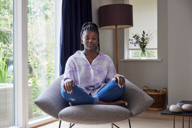 Peaceful Teenage Girl Meditating Sitting In Chair At Home stock photo