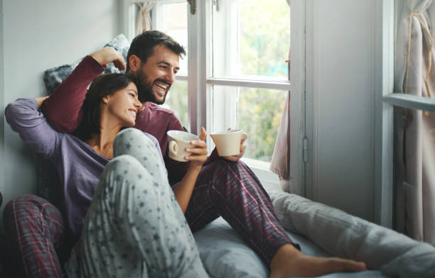 Peaceful weekend morning. Closeup side view of a mid 20's couple having some coffee and relaxing in bed on a lazy weekend morning. sunday morning coffee stock pictures, royalty-free photos & images