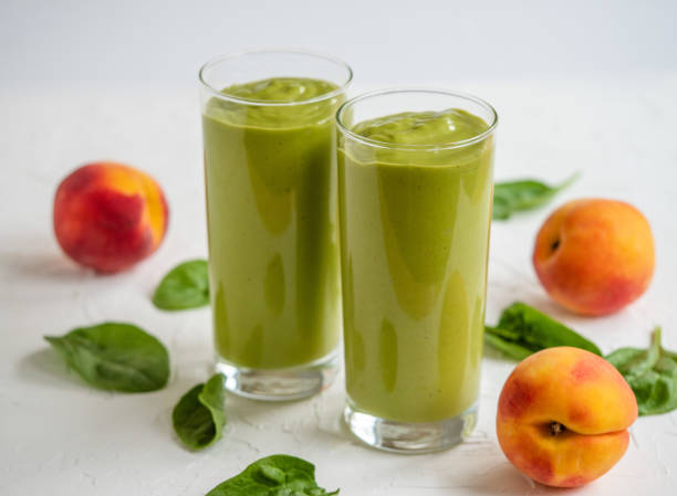 Peach and spinach smoothie Two glasses with green smoothie made from fresh peaches and spinach. peach smoothie stock pictures, royalty-free photos & images