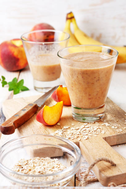 peach banana smoothie with oatmeal peach banana smoothie with oatmeal  in a glass,  fresh peaches on a wooden background peach smoothie stock pictures, royalty-free photos & images
