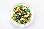 istock Peach, blueberry and arugula fresh fruit salad with cheese and almond nuts, top view 1395140920