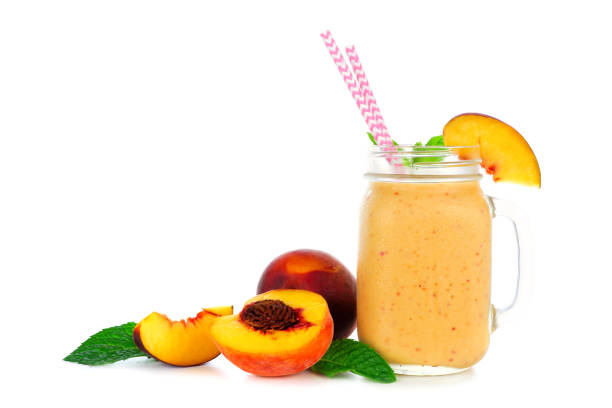 Peach smoothie in a mason jar glass with fruit isolated on white Peach smoothie in a mason jar glass with scattered fruit isolated on a white background peach smoothie stock pictures, royalty-free photos & images