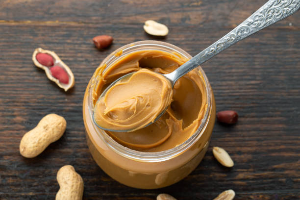 Peanut butter in an open jar and peanuts in the skin are scattered stock photo
