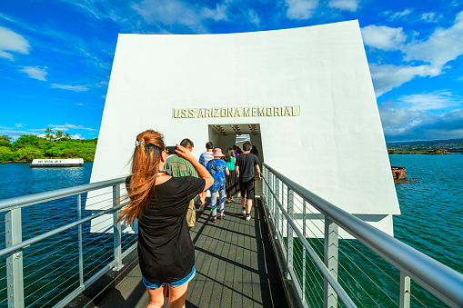 HONOLULU, OAHU, HAWAII, UNITED STATES - AUGUST 21, 2016: Tourists at the monument in honor of the USS Arizona BB-39 shipwreck of world war 2 in Pearl Harbor, with the American flag in memorial.