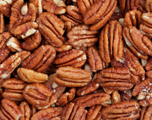 Pecan nuts background Background texture of pecan nuts showing the nuts in a natural state with perfect pecan halves and with cracked and broken ones. Space for text. pecan stock pictures, royalty-free photos & images