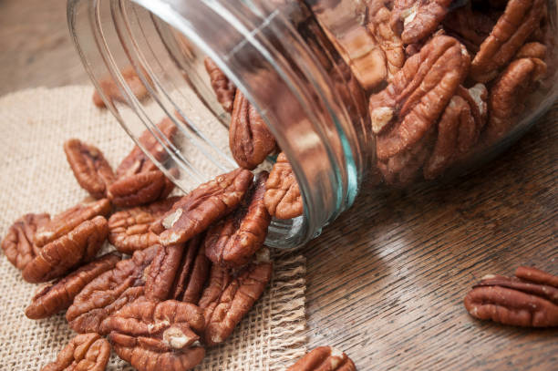 pecan nuts falling from glass container on wooden table background closeup of pecan nuts falling from glass container on wooden table background pecan stock pictures, royalty-free photos & images