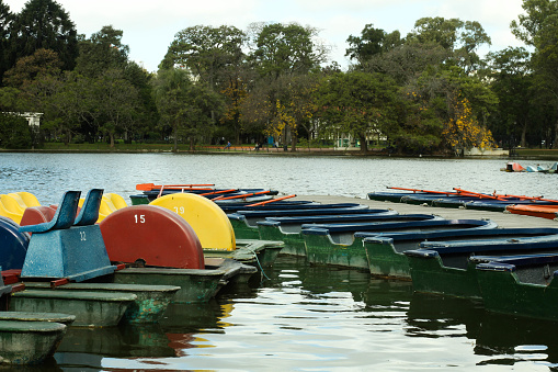 Lake sororunded by trees an vegetation\ncolorful boats to ride parked at the lake \nPalermo, Buenos Aires, argentina