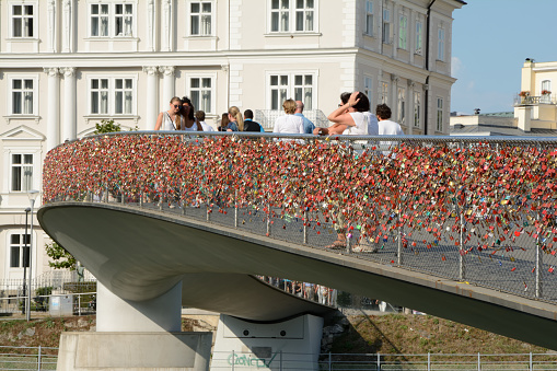 Salzburg, Austria - September 1, 2015: Pedestrian bridge with thousands of padlocks on barrier over Salzach river in Salzburg in Austria. Unidentified people visible.