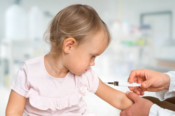 Pediatrician doctor is injecting vaccine to shoulder of baby stock photo