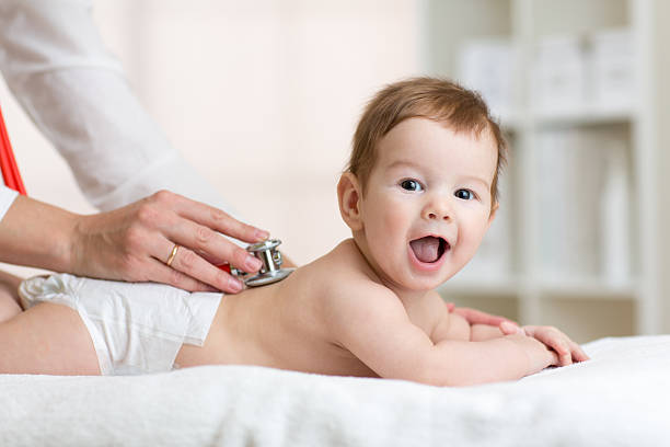 Pediatrician examining baby. Doctor using stethoscope listen to kid back stock photo