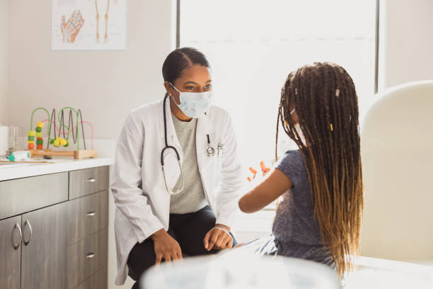 Pediatrician smiles through protective mask as young patient speaks stock photo