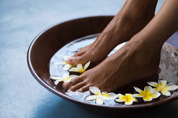 woman soaking chocolate skinned feet in a wooden bowl containing water and white-yellow flowers