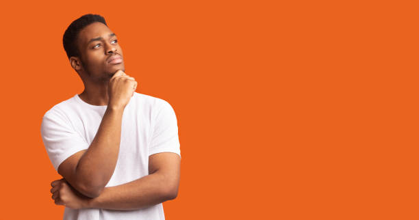 Pensive black man profile portrait on orange background Searching For Idea. Thoughtful african american guy looking up at free space, holding hand on chin, panorama uncertainty stock pictures, royalty-free photos & images
