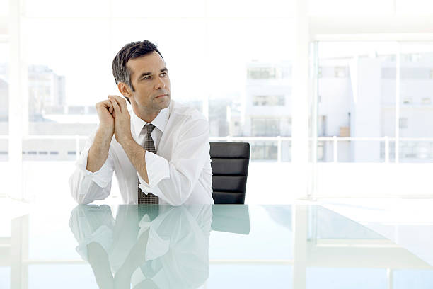 Pensive businessman sitting in board room Pensive business executive officer sitting alone in board room. and looking away cfo stock pictures, royalty-free photos & images