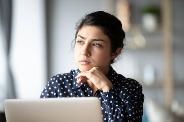 Pensive ethnic woman look in distance making decision Pensive young ethnic woman distracted from computer work look in window distance thinking, thoughtful millennial Indian girl lost in thoughts pondering solving problem, making decision introspection stock pictures, royalty-free photos & images