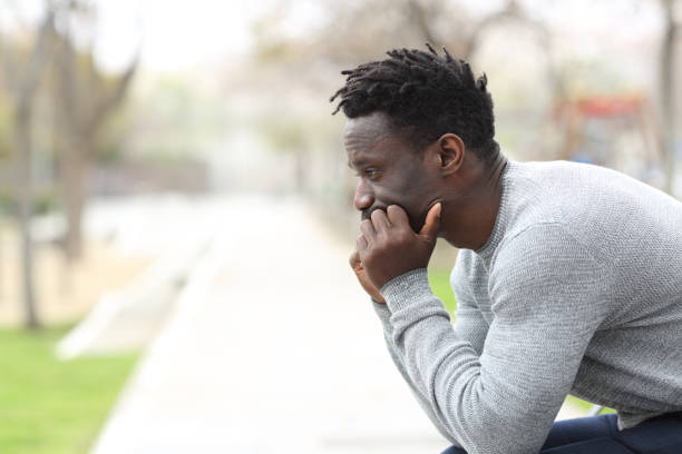 Pensive serious black man looking away on a park Side view portrait of a pensive serious black man looking away sitting on a park bench introspection stock pictures, royalty-free photos & images