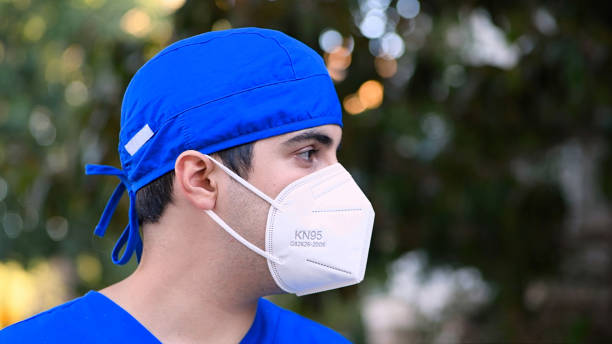 pensive yorgun genç erkek sağlık çalışanı bir n95 koruyucu yüz maskesi giyen uzağa bakıyor - n95 mask stok fotoğraflar ve resimler