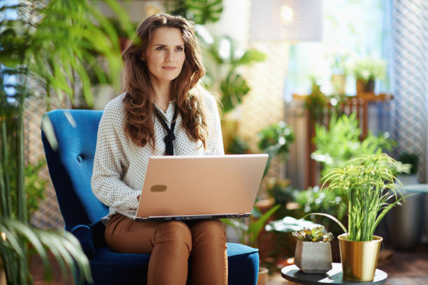 pensive trendy woman in modern house in sunny day using laptop stock photo