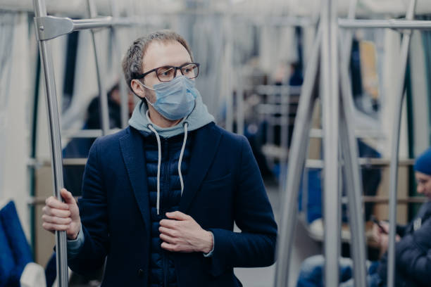pensive ung man i glasögon bär skyddande kirurgisk mask under coronavirus utbrott, utgör i kollektivtrafiken, tänker hur man kan övervinna sjukdomen. virusskydd, karantänkoncept. - public transport bildbanksfoton och bilder