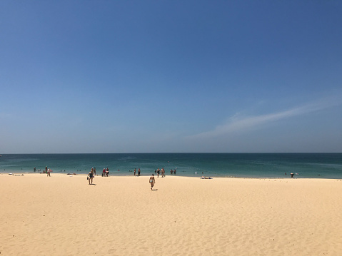 people are on the beach with clear sand, deep blue sea and bright blue sky in high season
