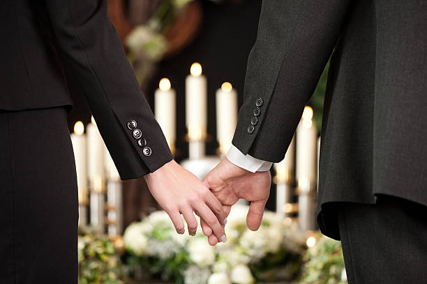 People at a funeral holding hands Religion, death and dolor  - couple at funeral holding hands consoling each other in view of the loss undertaker stock pictures, royalty-free photos & images