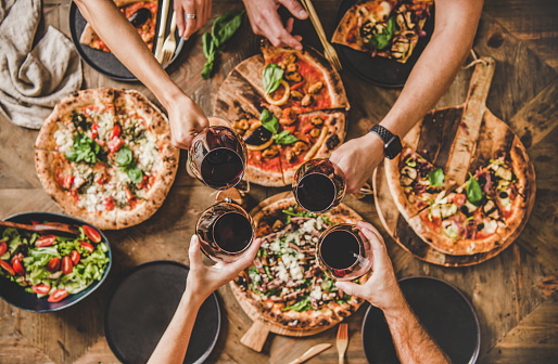 People clinking glasses with wine over table with Italian pizza