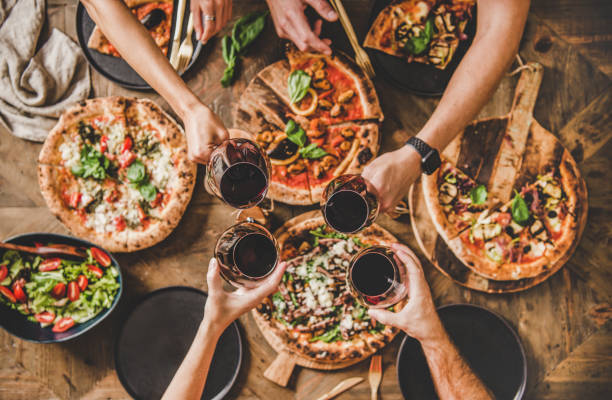 People clinking glasses with wine over table with Italian pizza Family or friends having pizza party dinner. Flat-lay of people clinking glasses with red wine over rustic wooden table with various kinds of Italian pizza, top view. Fast food lunch, celebration dough photos stock pictures, royalty-free photos & images