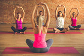 Beautiful sports people are sitting in lotus position and smiling while doing yoga with a trainer in modern fitness hall