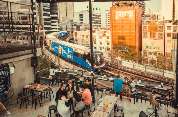 People drinking beer at open-air restaurant with urban cityscape and moving subway trains stock photo