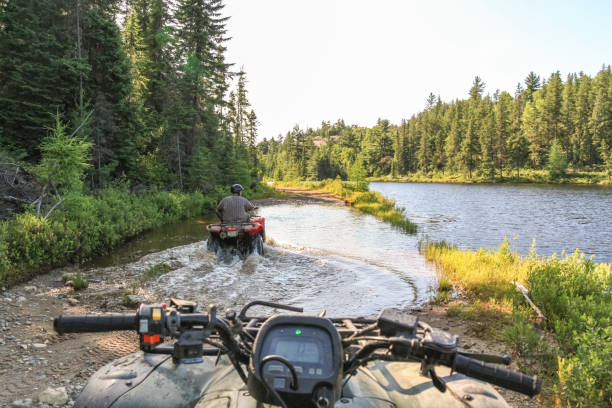 menschen, die atv-quads durch wasserdurchfahren. lake in ontario, kanada. - motorrad fluss stock-fotos und bilder