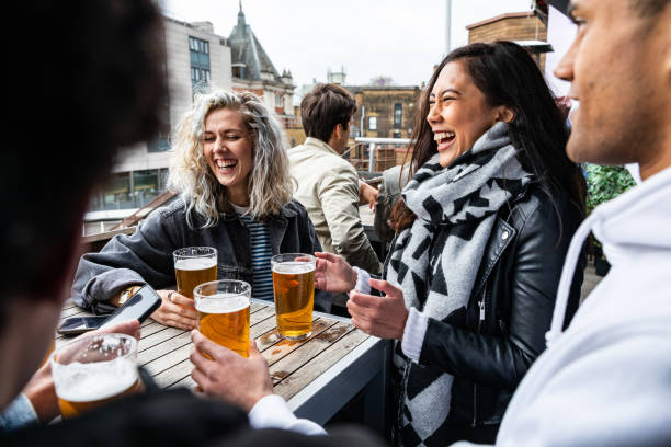 People enjoying a beer together at pub brewery - Happy laughing man and women talking and raising pint glass - Lifestyle and drink concepts in London stock photo