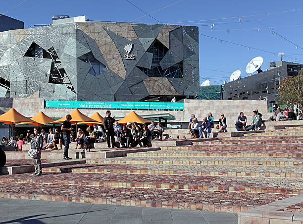 People enjoying the sunshine in Federation Square, Melbourne, Australia Melbourne, Australia - April 17 2011: People sitting on the steps at Federation Square, designed in 1997, with the distinctive architecture in the background. federation square stock pictures, royalty-free photos & images