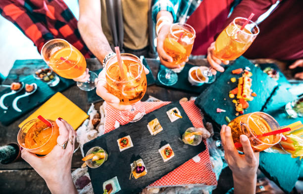 People hands toasting multicolored spritz drinks - Trendy friends having fun together drinking cocktails on happy hour at bar buffet - Social gathering party time concept on hipster orange filter stock photo