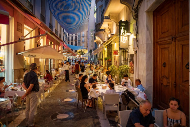 People have dinner in downtown Malaga Andalusia Spain People dine outdoors on moody alley patios in downtown Malaga, Andalusia, Spain on a pleasant evening. costa del sol málaga province stock pictures, royalty-free photos & images